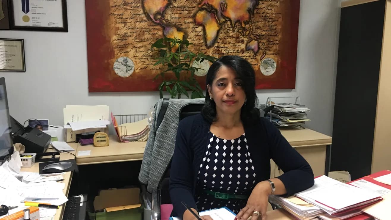 Woman in navy cardigan sitting at a desk with a large world map painting background.